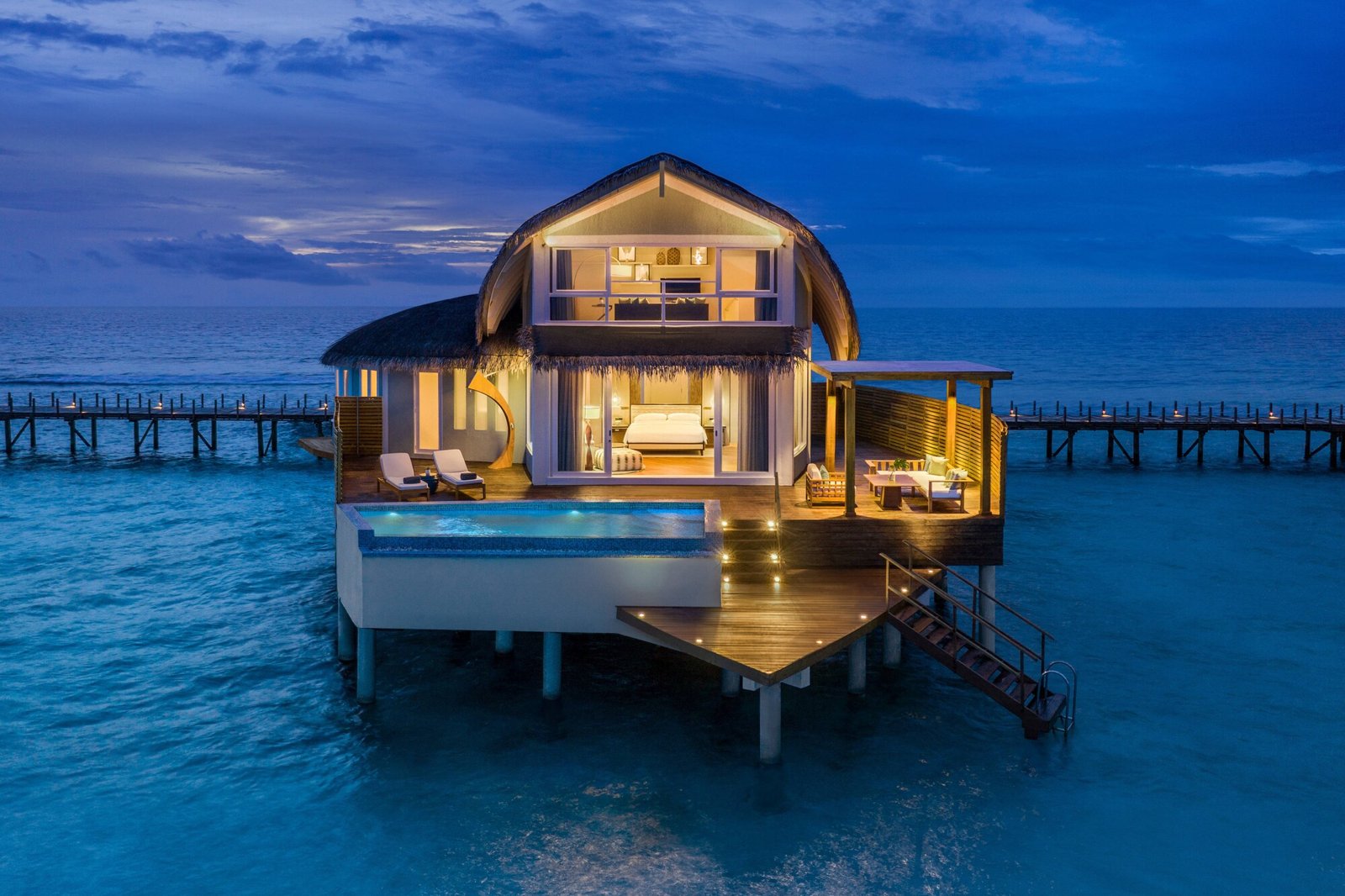 A warmly lit private overwater villa and pool at dusk in the Maldives